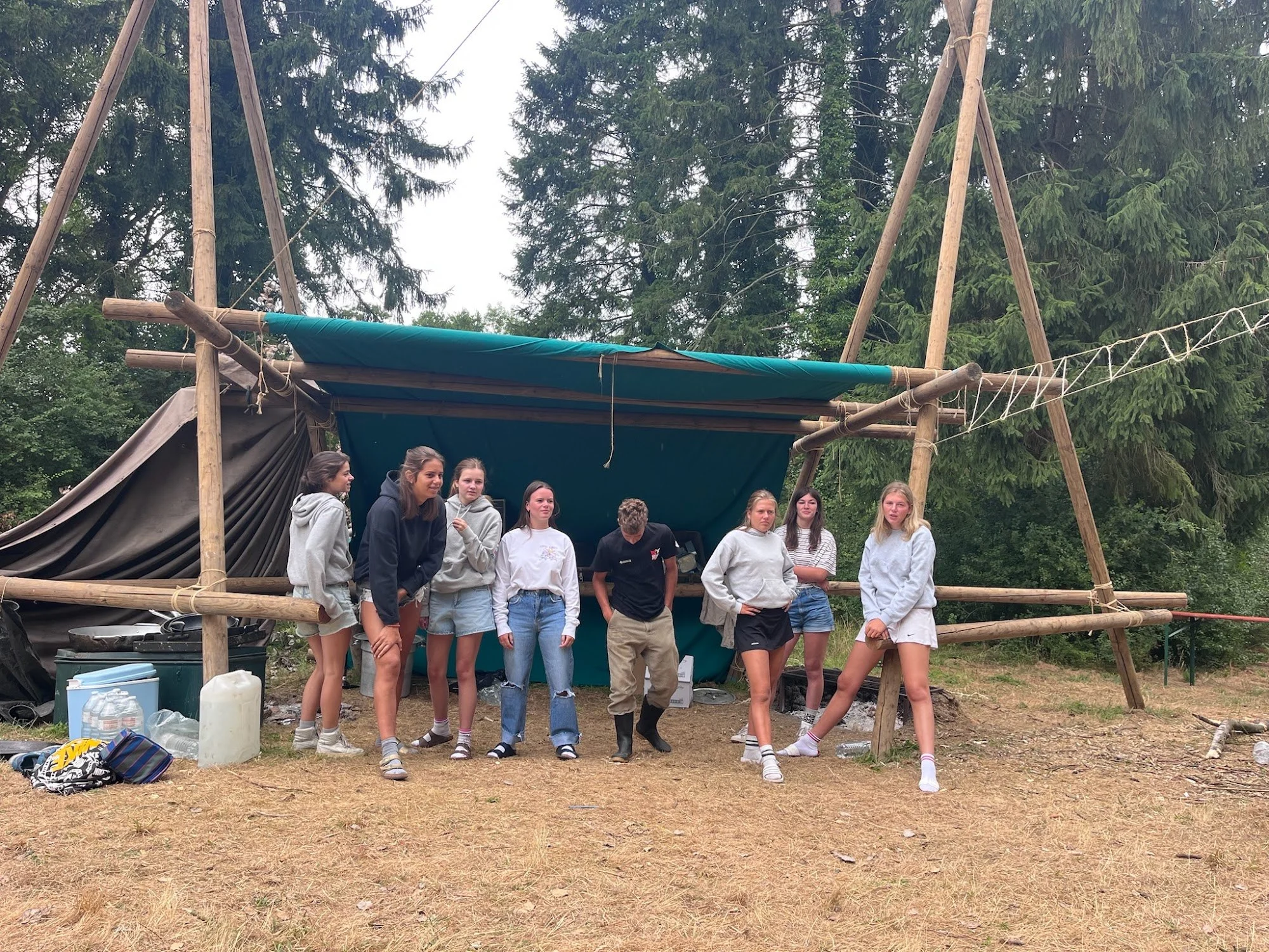 Givers staan voor een grote zelfgesjorde constructie met zeil, op kamp in het bos